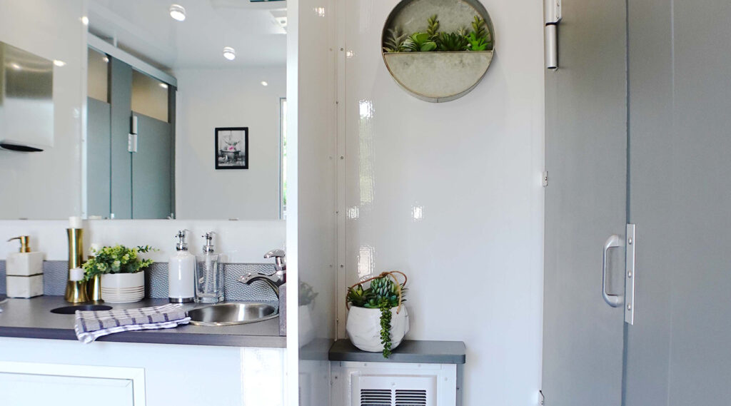 Interior shot of a luxury restroom trailer with gray stalls and greenery on the counter top