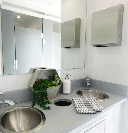Gray counter in a luxury restroom trailer with green plant and linen towel
