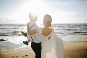 Groom carrying bride while walking on the beach on a sunny day